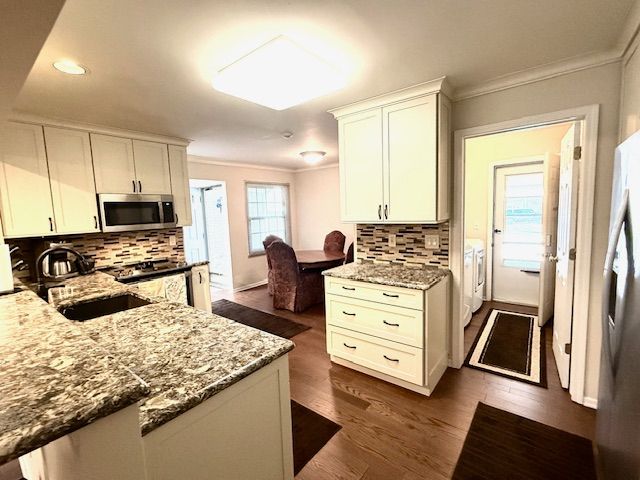kitchen featuring light stone countertops, appliances with stainless steel finishes, crown molding, and a sink