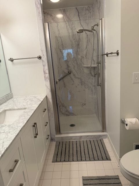 bathroom with tile patterned flooring, toilet, vanity, baseboards, and a marble finish shower