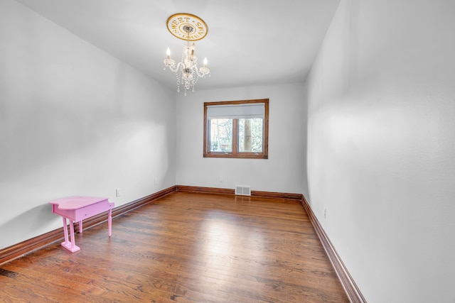spare room featuring a chandelier, visible vents, wood finished floors, and baseboards
