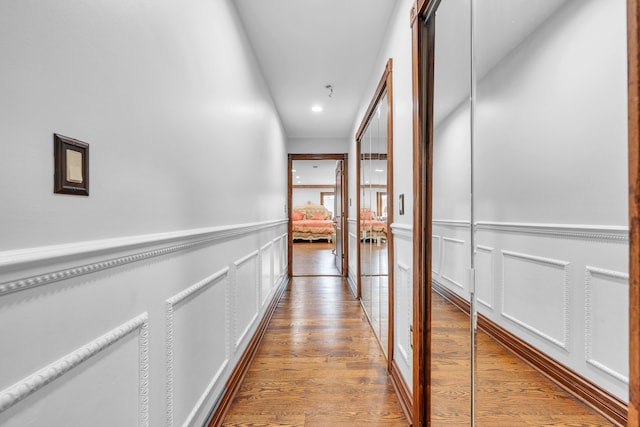 hallway with recessed lighting, a wainscoted wall, wood finished floors, and a decorative wall