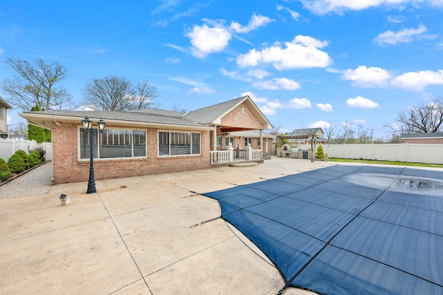 rear view of property with brick siding, a fenced backyard, a fenced in pool, and a patio area