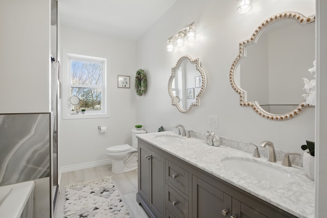 bathroom with double vanity, toilet, baseboards, and a sink