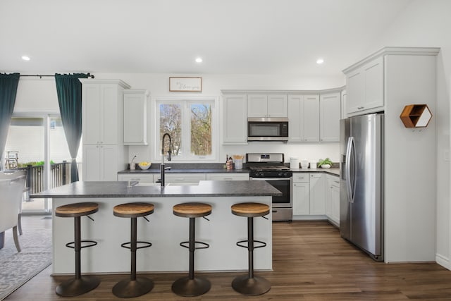 kitchen with recessed lighting, stainless steel appliances, dark countertops, and a kitchen bar
