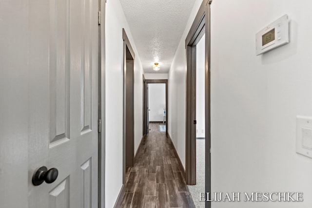hallway featuring dark wood finished floors, baseboards, and a textured ceiling
