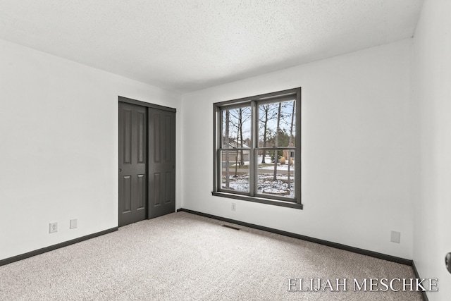 carpeted spare room featuring baseboards, visible vents, and a textured ceiling