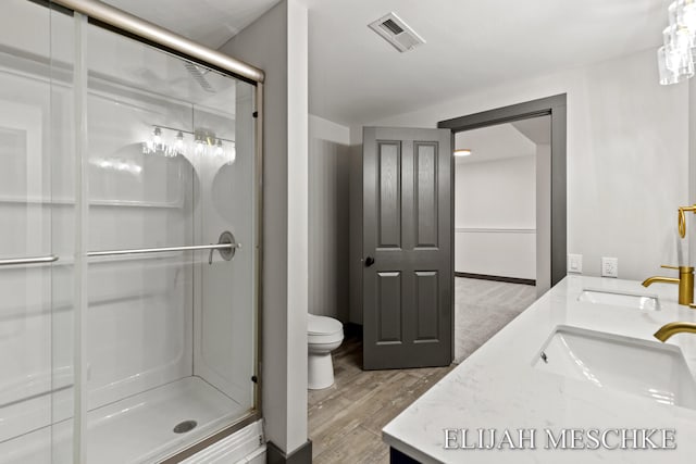 full bath featuring wood finished floors, a shower stall, double vanity, toilet, and visible vents