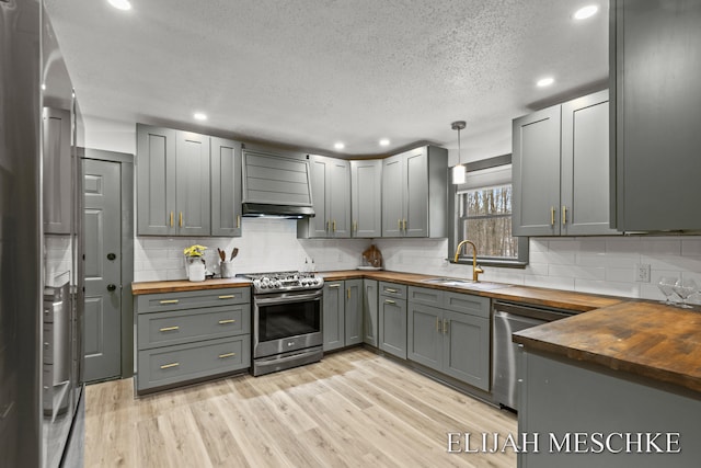 kitchen with appliances with stainless steel finishes, butcher block countertops, light wood finished floors, and a sink