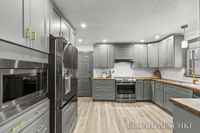 kitchen with gray cabinets, butcher block counters, appliances with stainless steel finishes, a sink, and light wood-type flooring