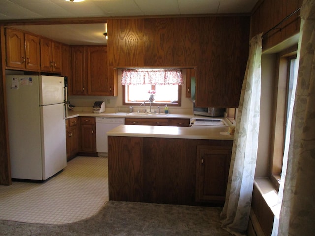 kitchen with brown cabinets, a sink, white appliances, a peninsula, and light countertops