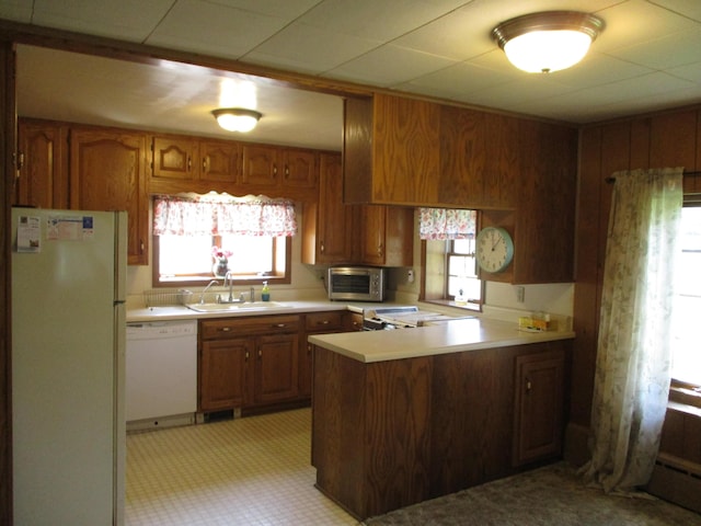kitchen featuring white appliances, light countertops, brown cabinets, a sink, and a peninsula