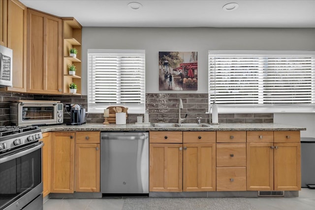 kitchen with backsplash, appliances with stainless steel finishes, a sink, a toaster, and stone countertops