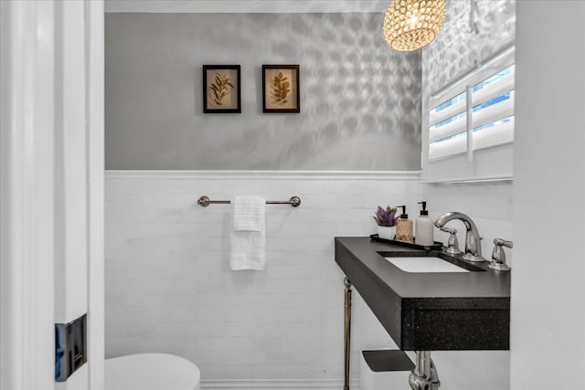 half bathroom featuring tile walls, wainscoting, vanity, toilet, and a notable chandelier