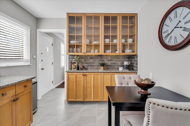 kitchen with light stone counters, decorative backsplash, and glass insert cabinets