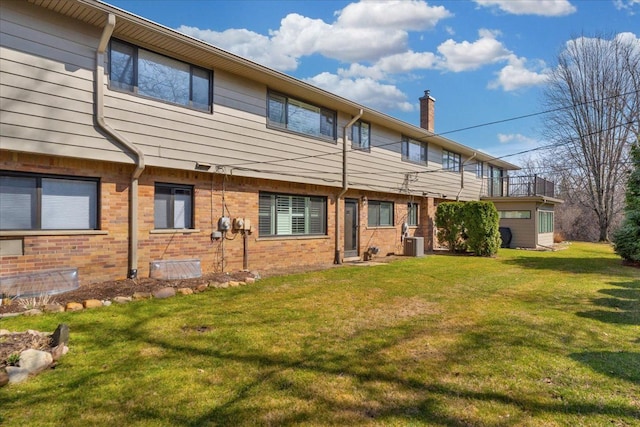 back of property with brick siding, central AC unit, a yard, and a chimney
