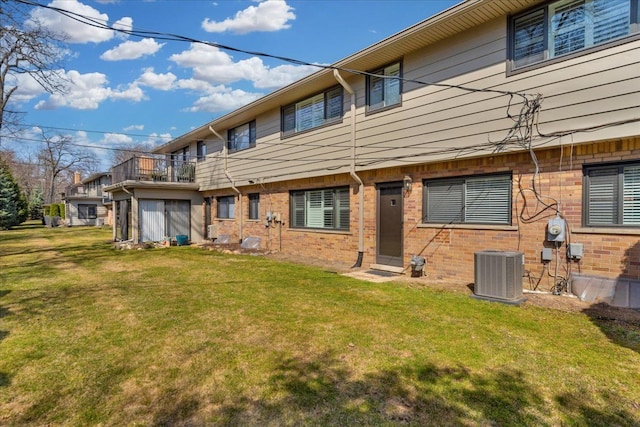 rear view of house featuring a lawn, cooling unit, a balcony, and brick siding