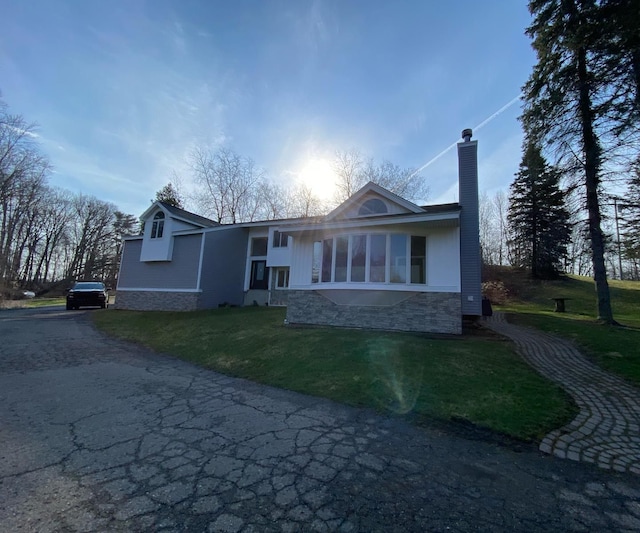 back of property featuring a chimney, driveway, a lawn, and stone siding