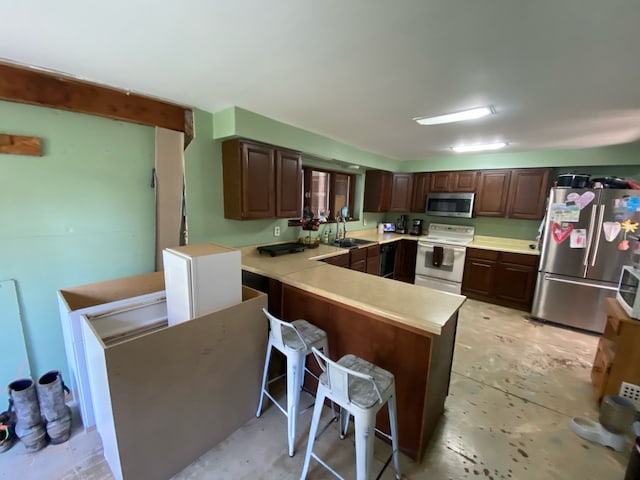 kitchen featuring a sink, a breakfast bar, a peninsula, light countertops, and appliances with stainless steel finishes