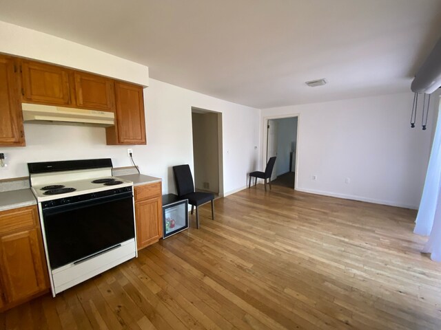 kitchen featuring under cabinet range hood, electric range oven, brown cabinetry, light countertops, and hardwood / wood-style floors