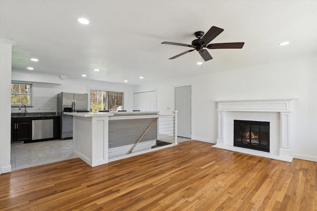 unfurnished living room with a sink, light wood-style floors, a glass covered fireplace, recessed lighting, and a ceiling fan