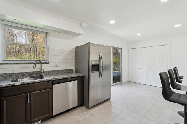 kitchen featuring dark brown cabinetry, appliances with stainless steel finishes, ornamental molding, backsplash, and a sink