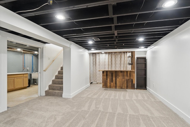finished basement with a bar, baseboards, light carpet, and stairs