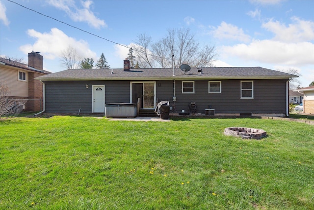 rear view of property featuring fence, an outdoor fire pit, a yard, and a hot tub