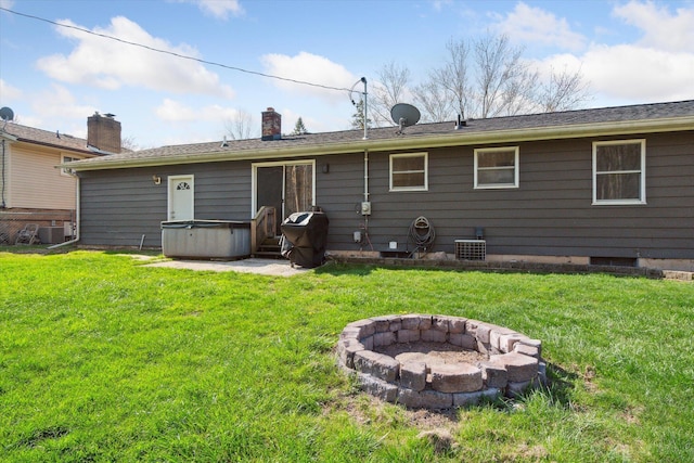 back of property featuring cooling unit, an outdoor fire pit, a yard, and a hot tub