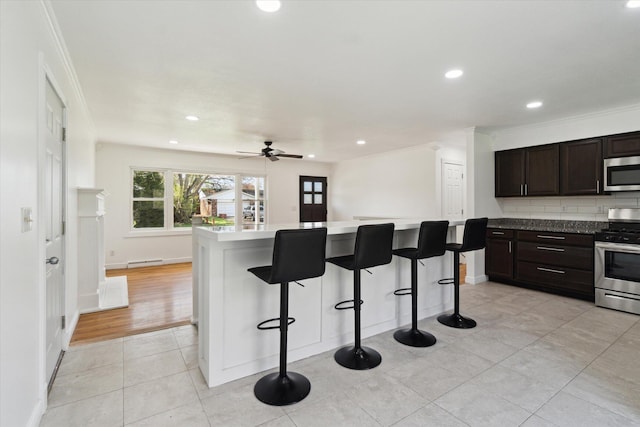 kitchen with light tile patterned floors, ceiling fan, a breakfast bar area, ornamental molding, and appliances with stainless steel finishes