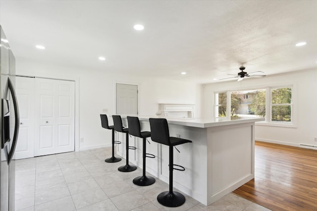 kitchen featuring recessed lighting, stainless steel fridge, a breakfast bar, a ceiling fan, and light countertops