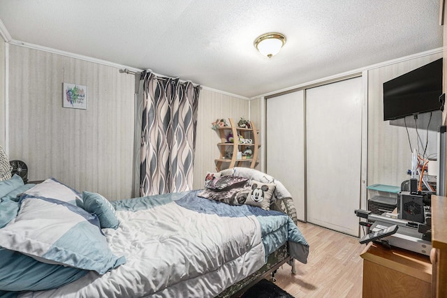 bedroom with a textured ceiling, crown molding, a closet, and light wood-style flooring