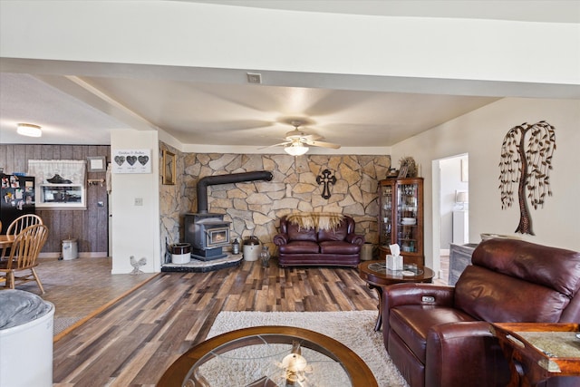 living area with baseboards, a wood stove, a ceiling fan, and wood finished floors