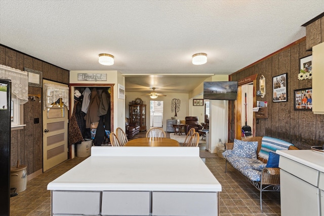 interior space with wooden walls, a ceiling fan, a textured ceiling, and light countertops