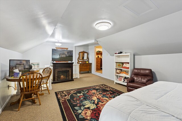 carpeted bedroom featuring baseboards, a warm lit fireplace, vaulted ceiling, and attic access