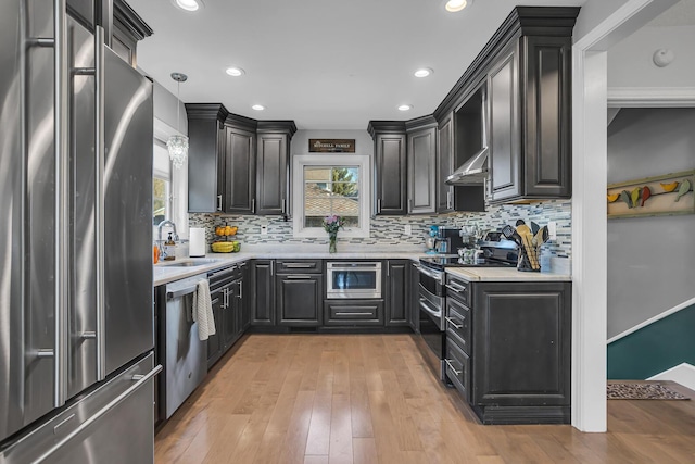 kitchen with stainless steel appliances, wall chimney exhaust hood, light countertops, and a sink
