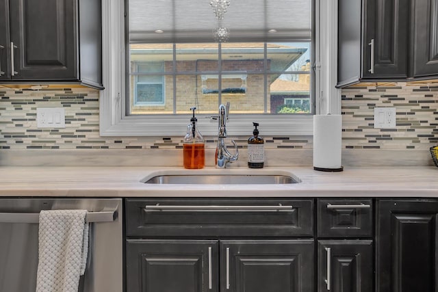kitchen featuring decorative backsplash, a sink, light countertops, dishwasher, and dark cabinetry