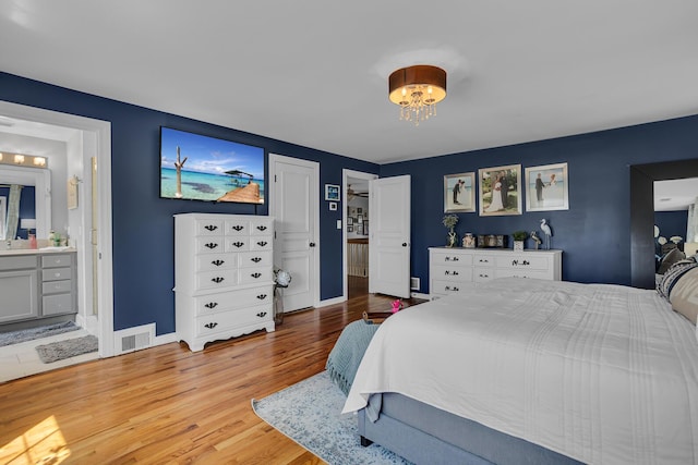 bedroom with a notable chandelier, visible vents, baseboards, wood finished floors, and ensuite bathroom