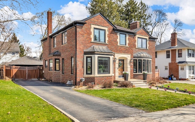 view of front facade with brick siding, fence, a front lawn, and a chimney