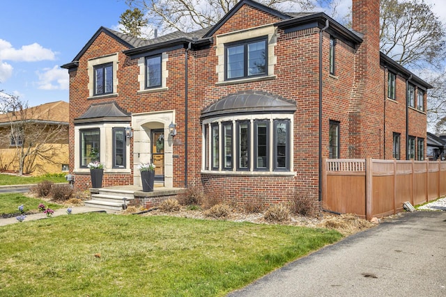 view of front of house featuring a chimney, brick siding, and a front yard