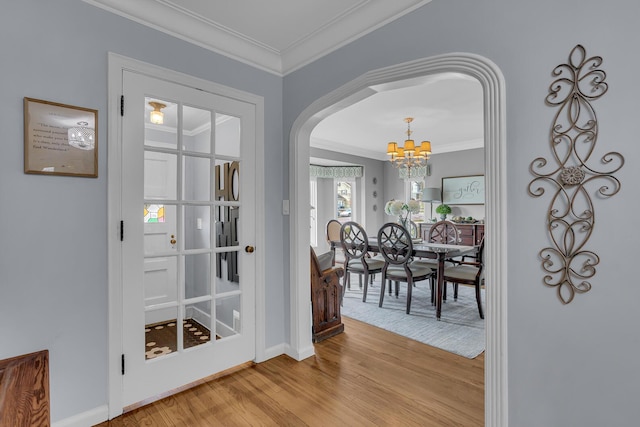 entryway featuring light wood-style floors, crown molding, a notable chandelier, and arched walkways