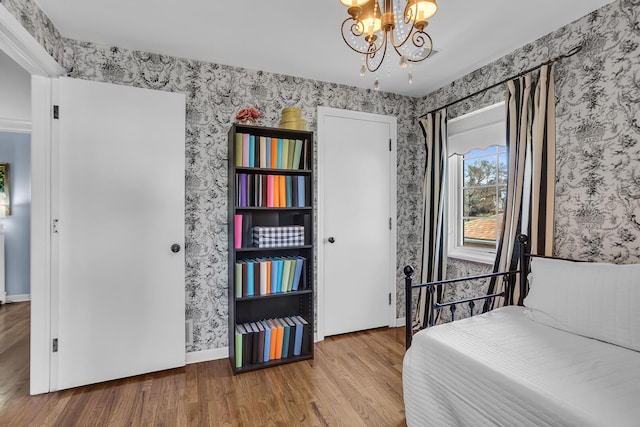bedroom featuring wallpapered walls, wood finished floors, and a notable chandelier