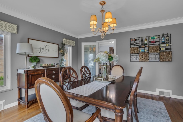 dining space featuring wood finished floors, baseboards, visible vents, a notable chandelier, and crown molding