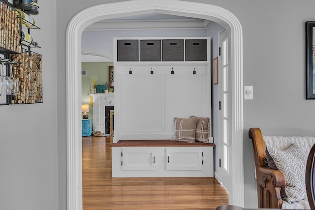 mudroom featuring wood finished floors, crown molding, arched walkways, and a fireplace