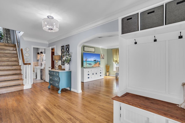 interior space featuring a notable chandelier, light wood-type flooring, baseboards, ornamental molding, and arched walkways