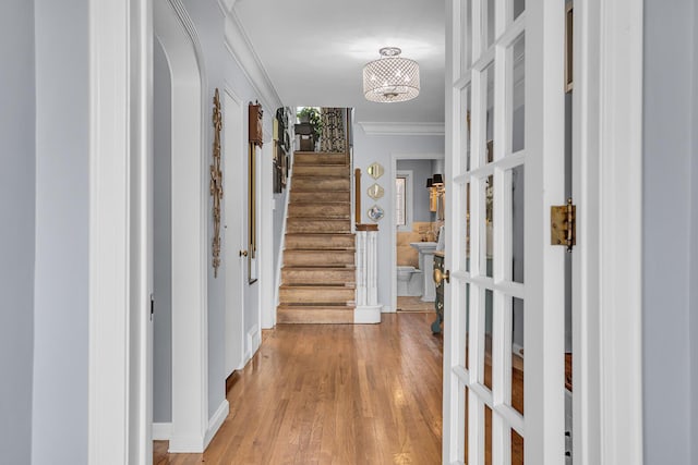 corridor with light wood-style floors, baseboards, ornamental molding, and stairs