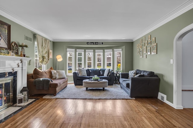 living room featuring crown molding, visible vents, a premium fireplace, arched walkways, and wood finished floors
