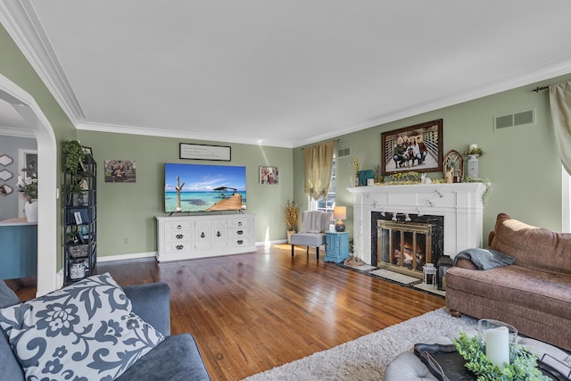 living room featuring arched walkways, wood finished floors, ornamental molding, a fireplace, and visible vents