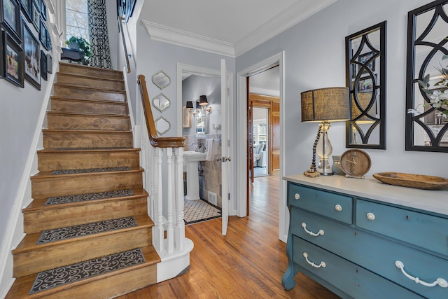 stairway with wood finished floors and ornamental molding