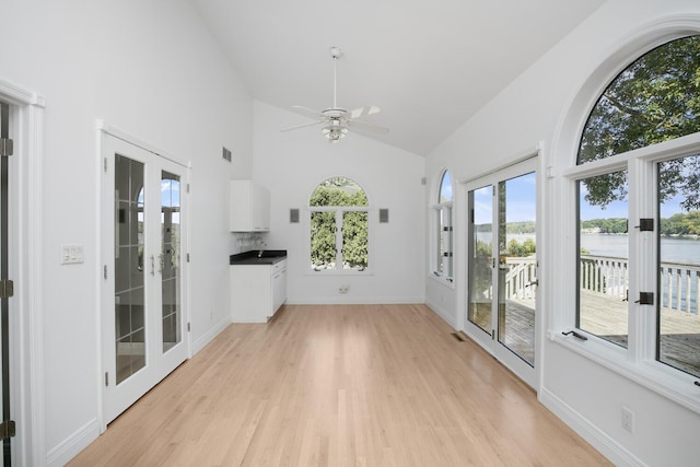 unfurnished living room featuring a healthy amount of sunlight, high vaulted ceiling, light wood-type flooring, and french doors