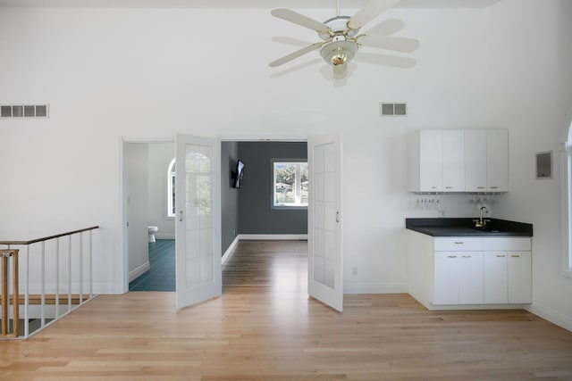 interior space with visible vents, light wood-type flooring, a ceiling fan, and white cabinets