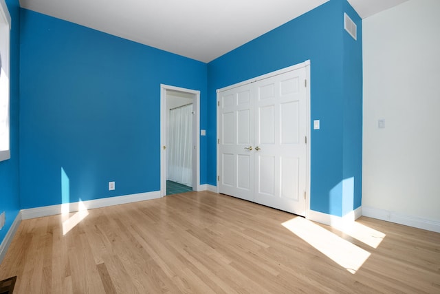 unfurnished bedroom featuring baseboards, visible vents, wood finished floors, and a closet
